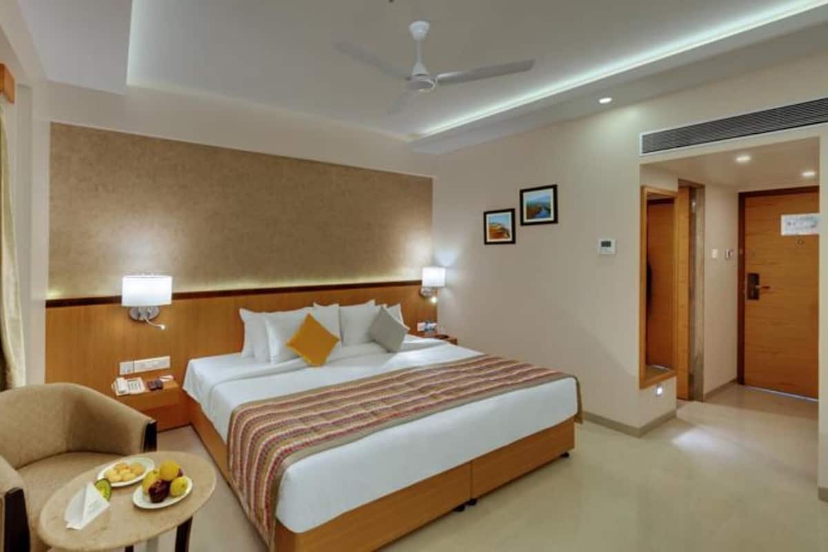 Una habitación de hotel con una cama, lámparas de noche, una silla y una mesita, y un ventilador de techo.