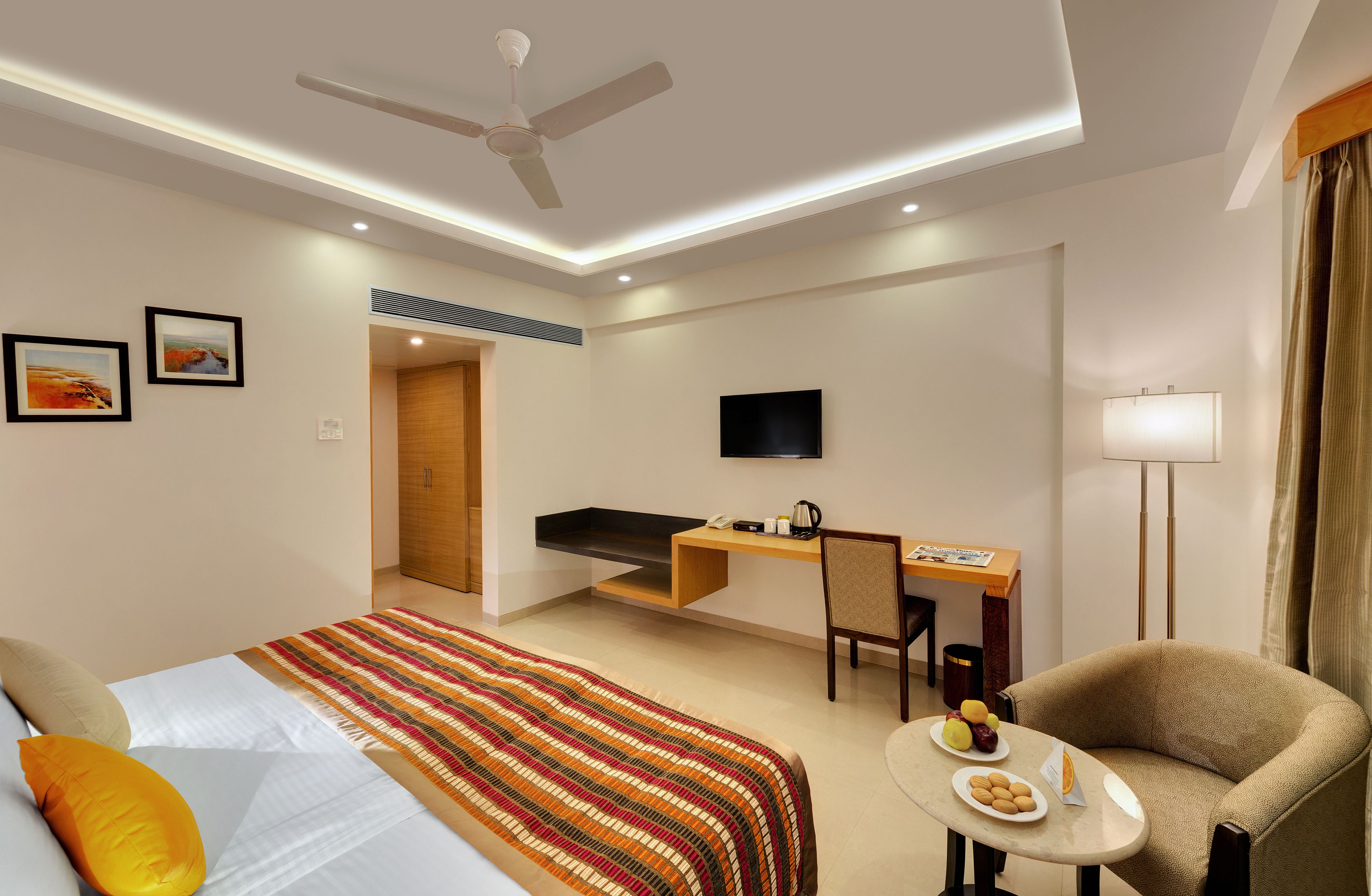 A hotel room with a bed, a desk, a chair, a television, and a small table with food.