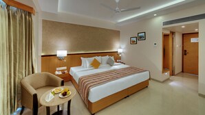 A hotel room with a bed, bedside table, chair, and a small table with fruits. - The Fern Residency, MIDC - Pune (Pune)