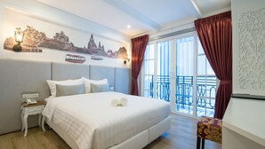 A hotel room with a large bed, a nightstand with a phone, a window with curtains, and a balcony with chairs. - White Ivory Bed & Breakfast (Bangkok)