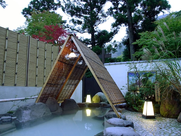 Un jardín japonés tradicional con una fuente de agua de piedra, estructuras de bambú y faroles.