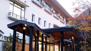 A modern hotel with a covered entrance, multiple floors, and a balcony with railings. - Kinokuniya Ryokan (Hakone)