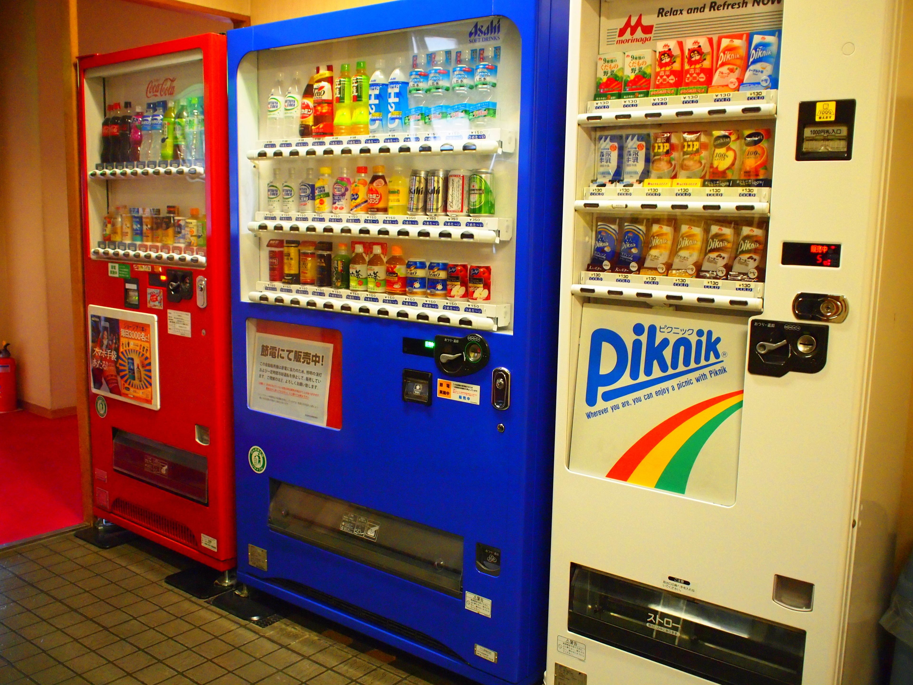 Três máquinas de venda automática com várias bebidas e lanches.