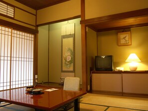 A traditional Japanese room with tatami flooring, a low table with a chair, a television, and a lamp. - Kinokuniya Ryokan (Hakone)