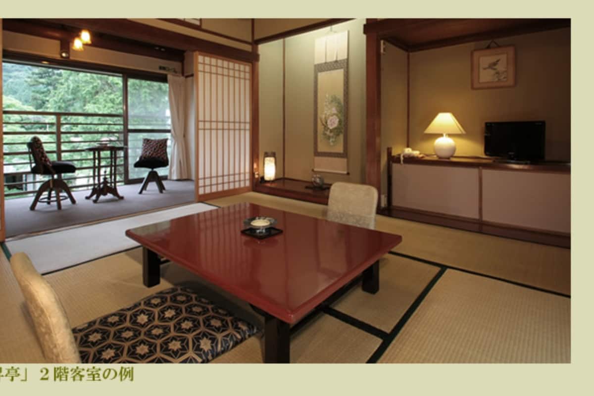 A traditional Japanese-style room with tatami flooring, a low table, and a view of a garden.