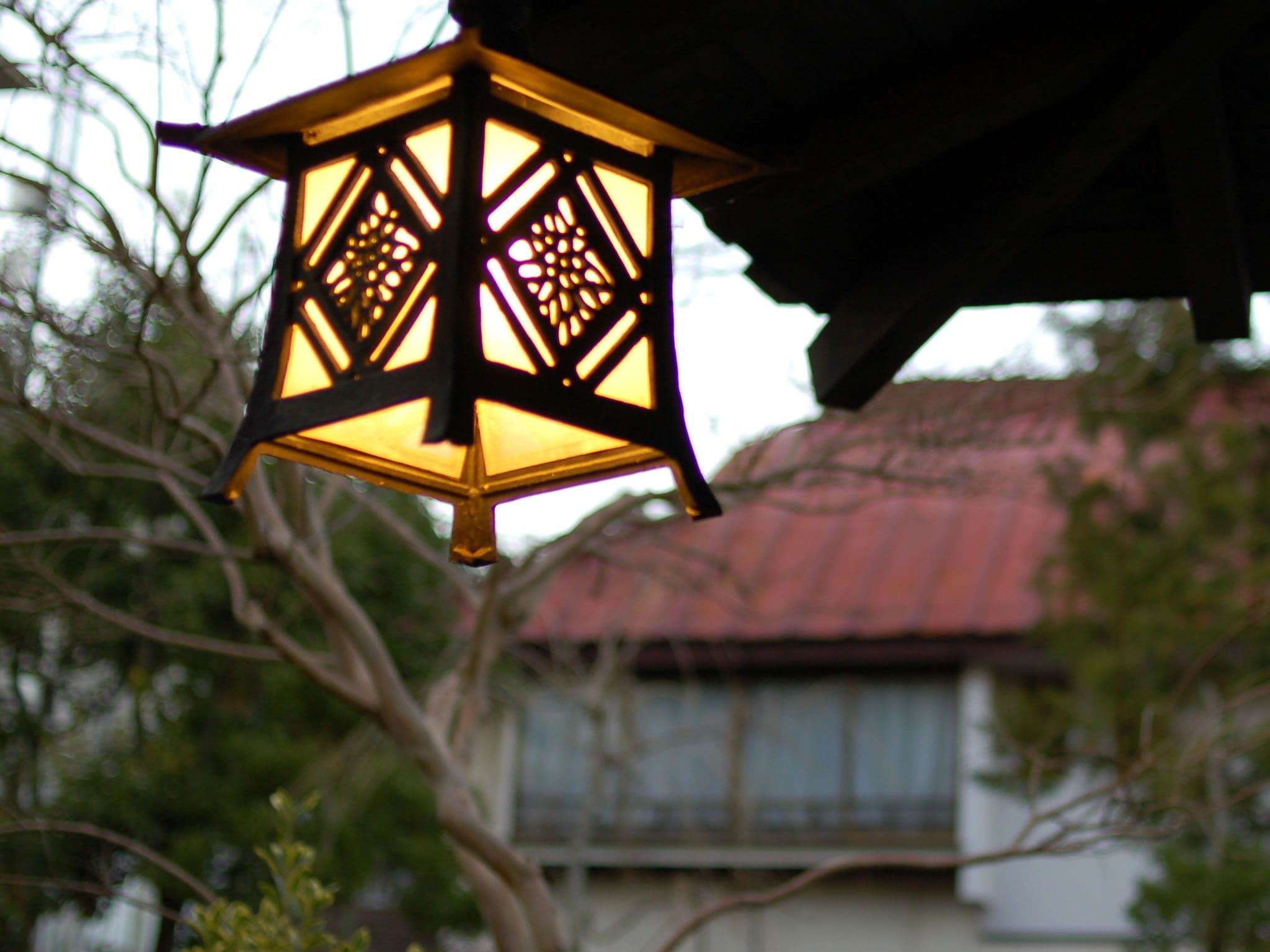 A hanging lantern with a geometric pattern, a red-roofed building, and trees in the background.