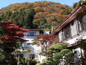 A traditional Japanese-style building with a sloped roof and wooden balcony, surrounded by lush greenery and autumn-colored trees. - Kinokuniya Ryokan (Hakone)
