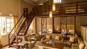 Ein geräumiges Hotelzimmer mit einer großen Sofaecke, einer Holztreppe und einem Etagenbett.