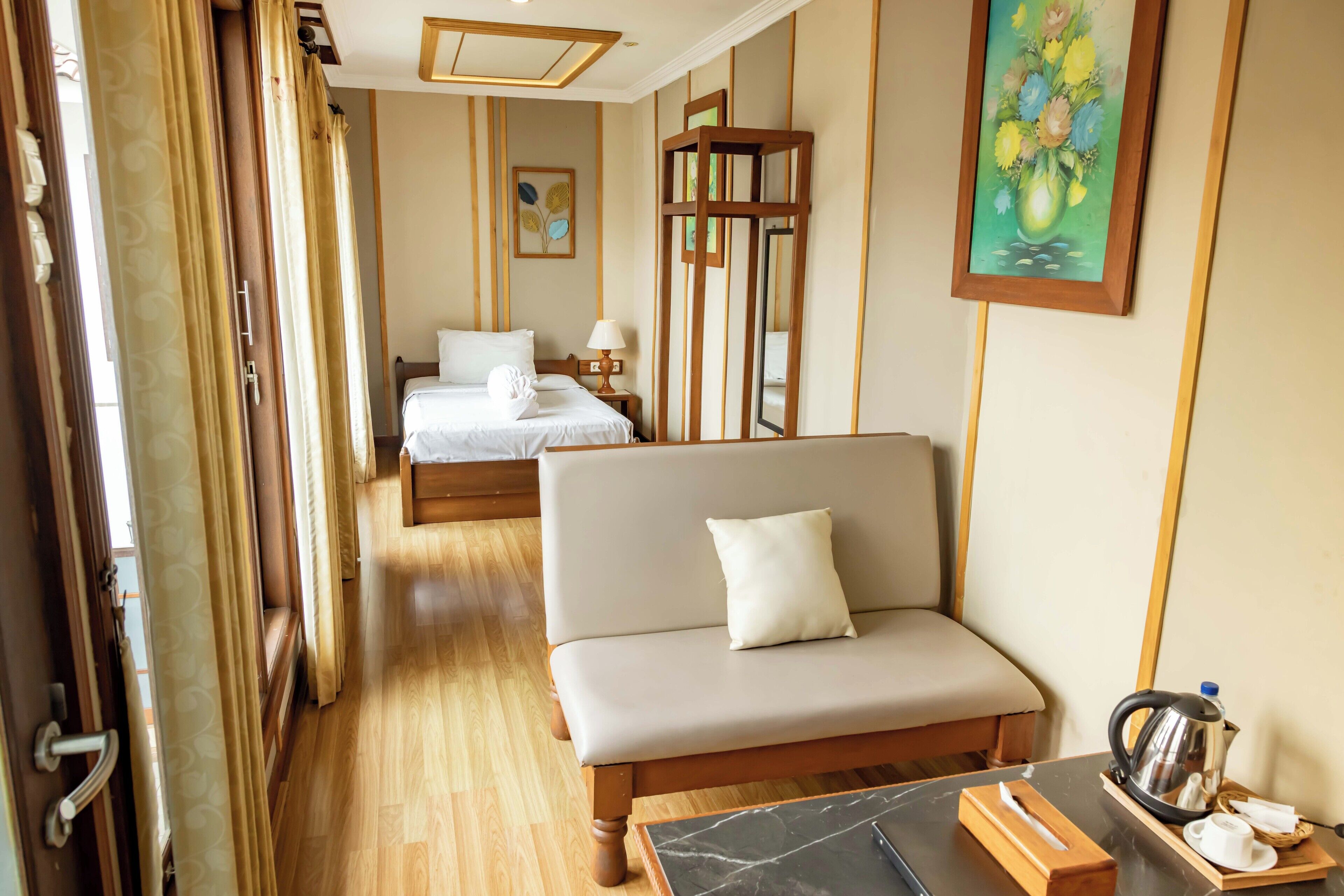 A hotel room with a bed, a sofa, a table with a kettle, and a painting on the wall.