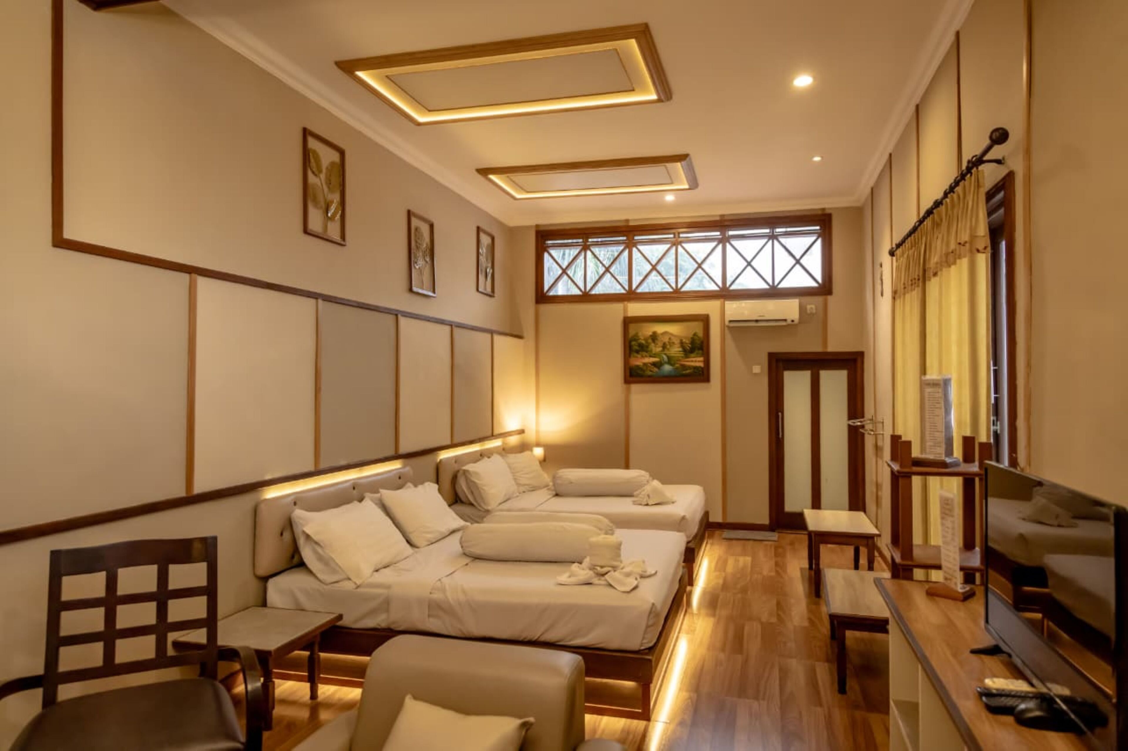 A hotel room with a wooden floor, a sofa bed, a TV, and a small table.