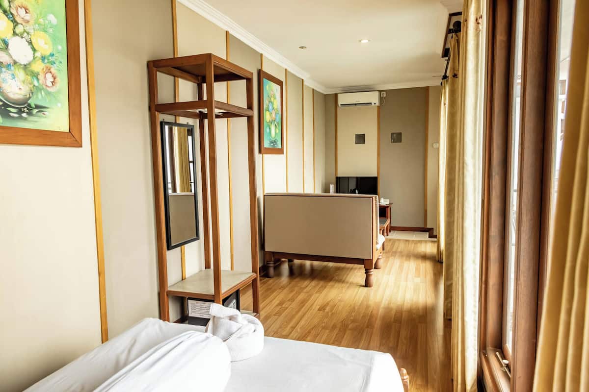 Hotellihuone, jossa on sänky, puinen tuoli, työpöytä ja suuri ikkuna, jossa on verhot.