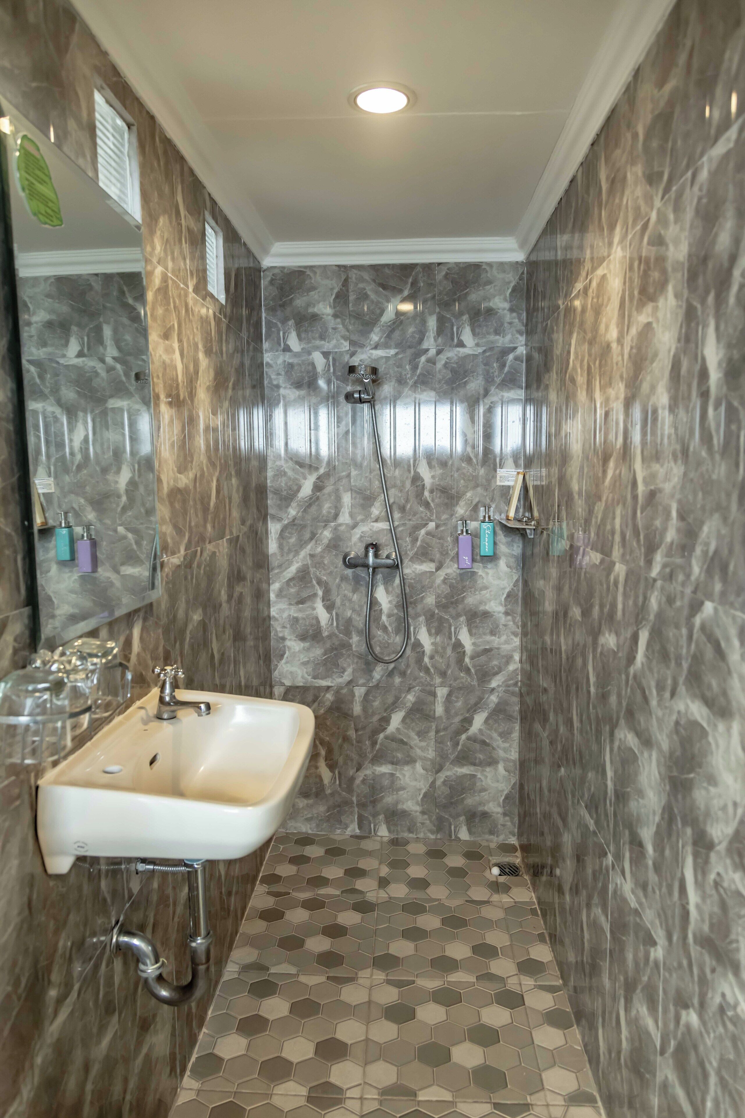 A bathroom with a marble shower wall, a sink with a mirror, and a tiled floor.