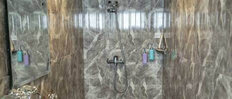 A bathroom with a marble shower wall, a sink with a mirror, and a tiled floor.