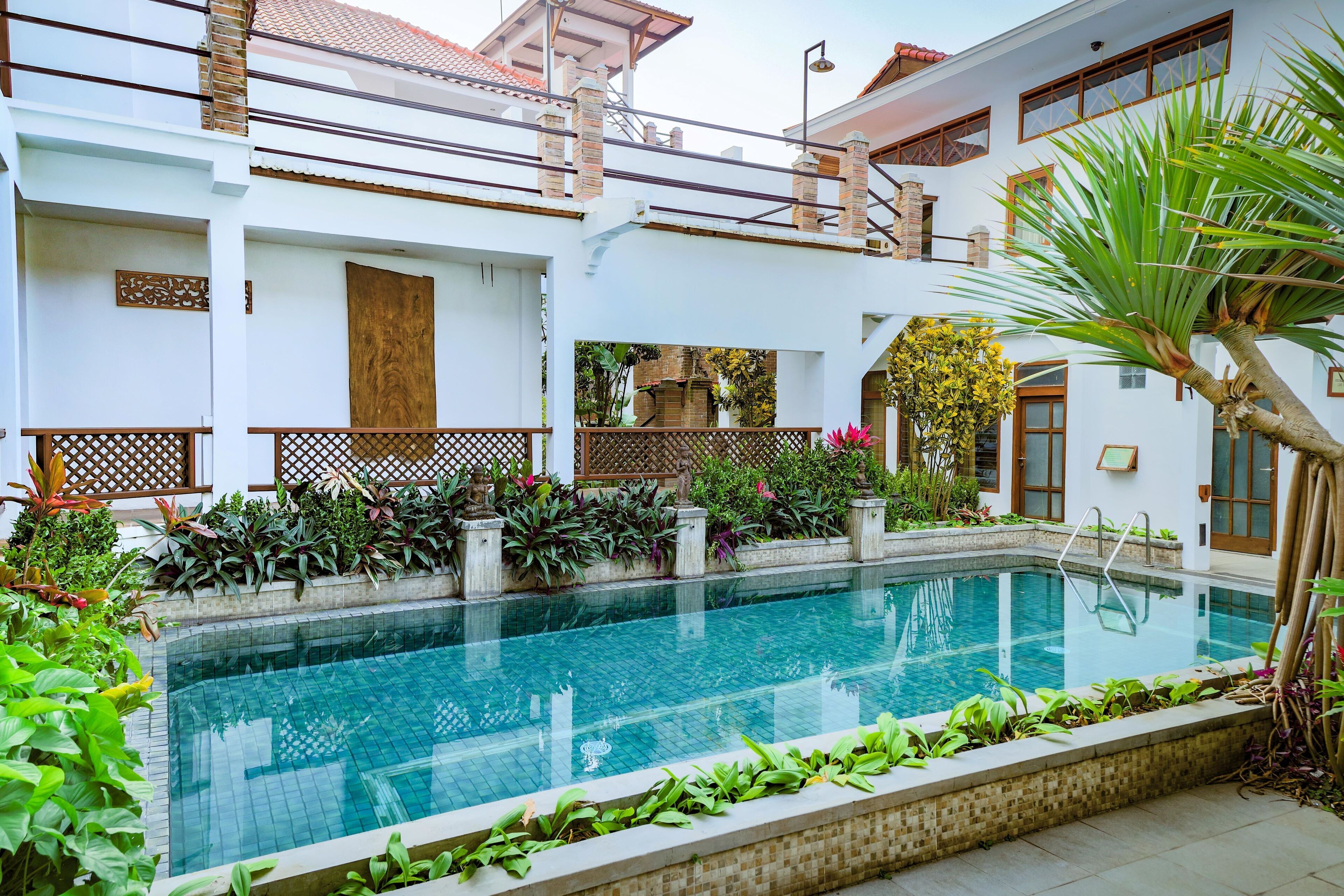 A swimming pool surrounded by lush greenery and a white building with a balcony.