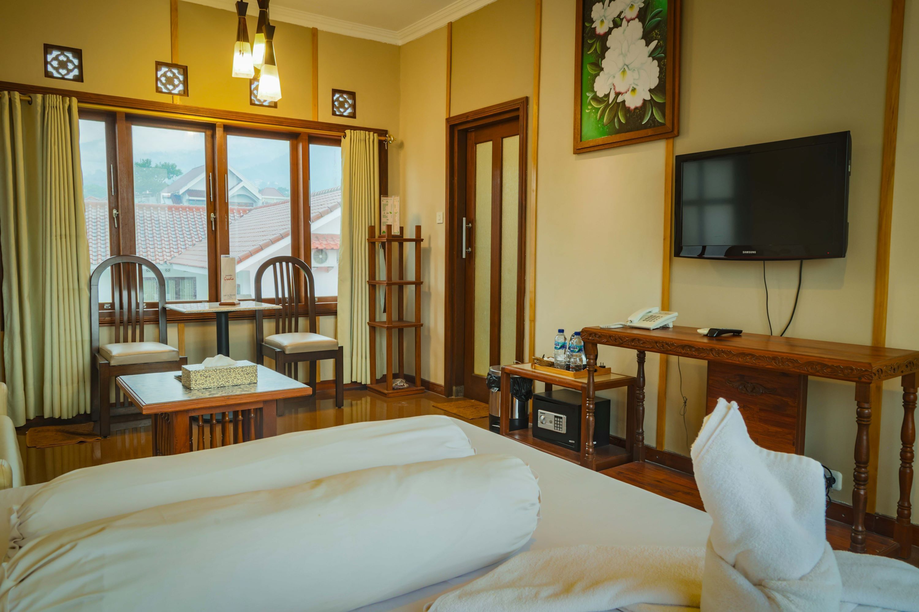 A hotel room with a bed, a desk with a telephone, a television, and a view of the outside.