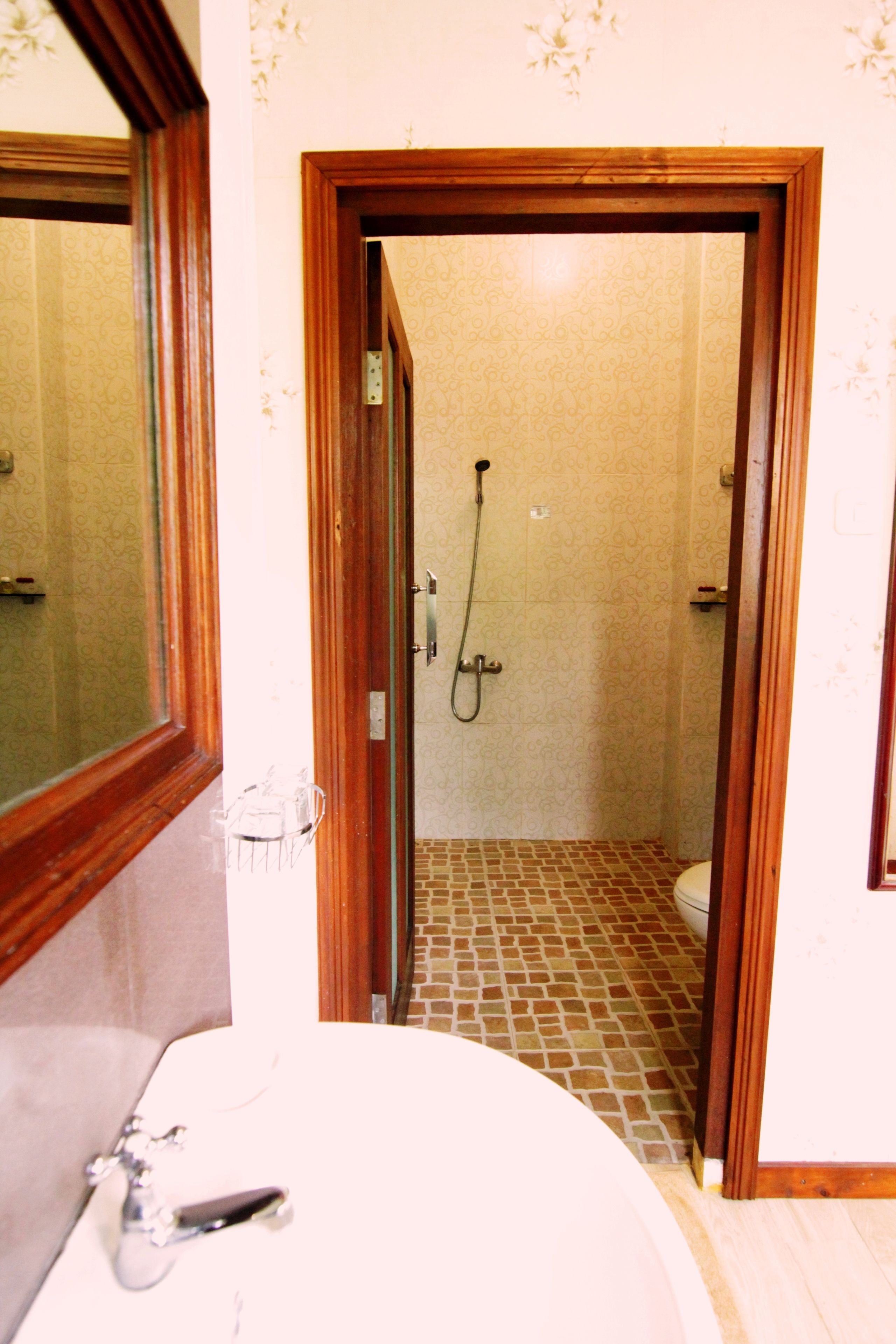 Un baño con puerta de madera que da a la zona de ducha, un lavabo y un espejo.