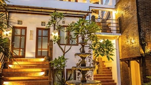 A two-story house with a well-lit entrance, a small fountain, and a staircase leading to the upper floor. - Hotel Gradia 2 (Batu)