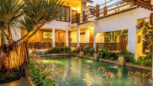 A courtyard with a pool, surrounded by lush greenery and a well-lit building with multiple balconies. - Hotel Gradia 2 (Batu)