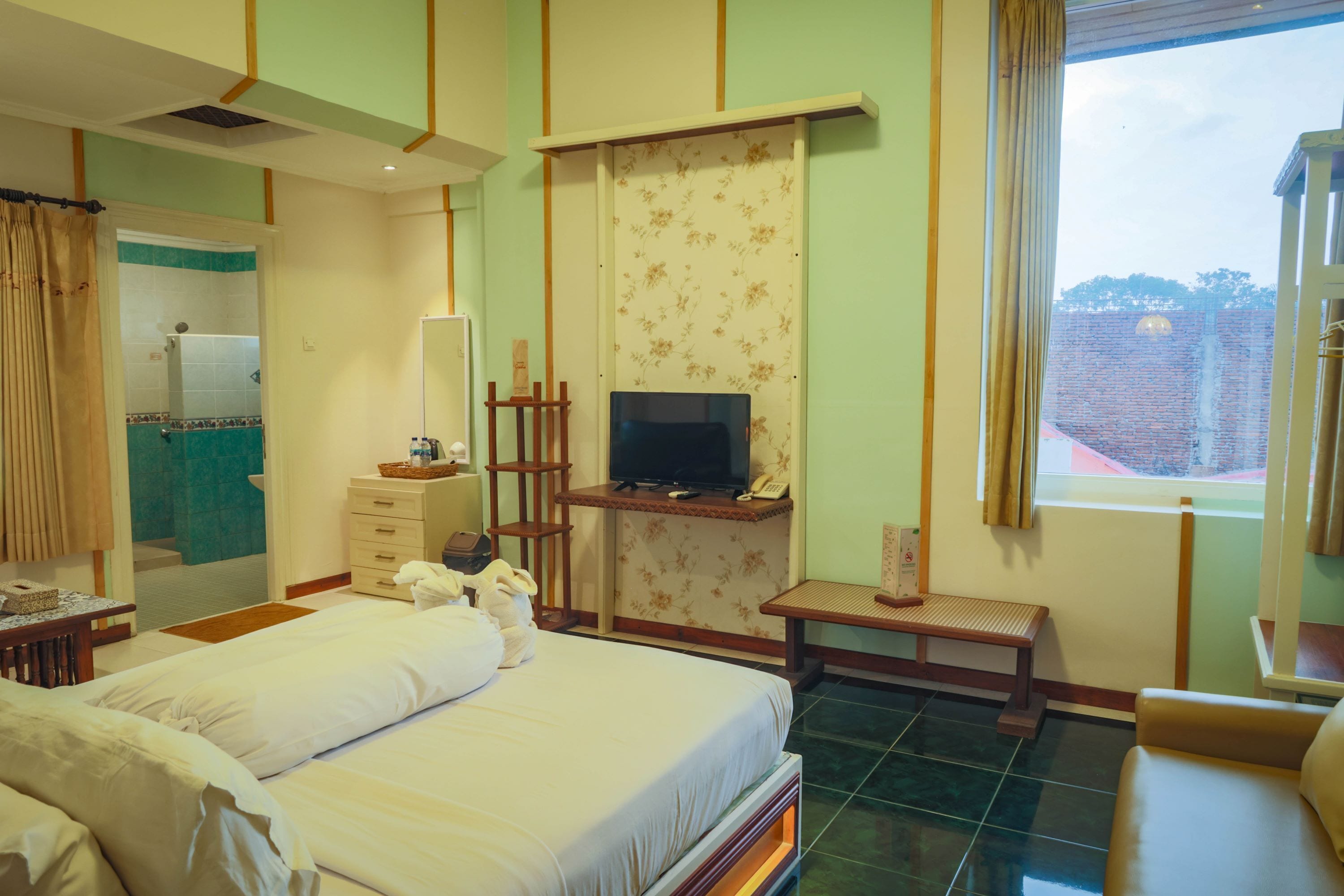 A hotel room with a bed, a TV, a desk, and a window with a view of a brick building.