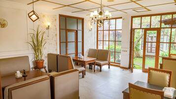 A cozy room with wooden furniture, a potted plant, and large windows offering a view of the outdoors.