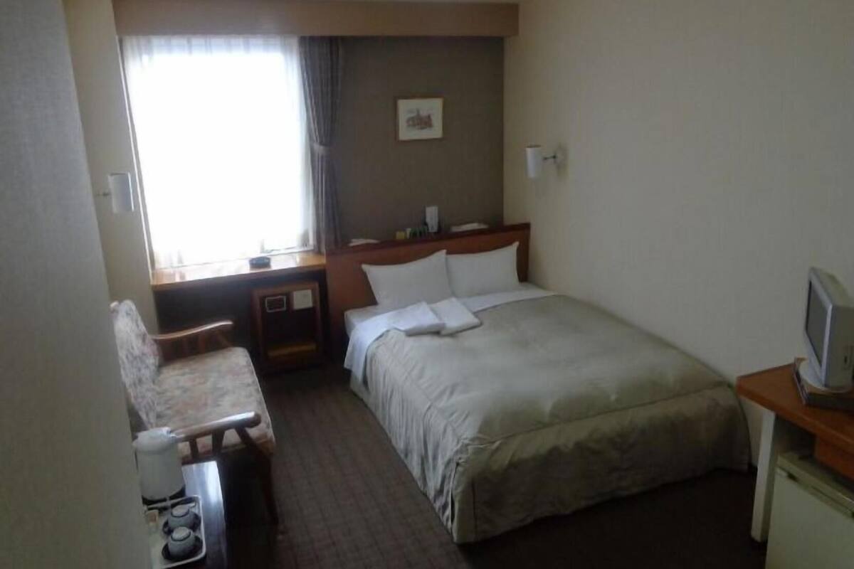 A hotel room with a bed, a desk, a chair, a television, and a window with curtains.