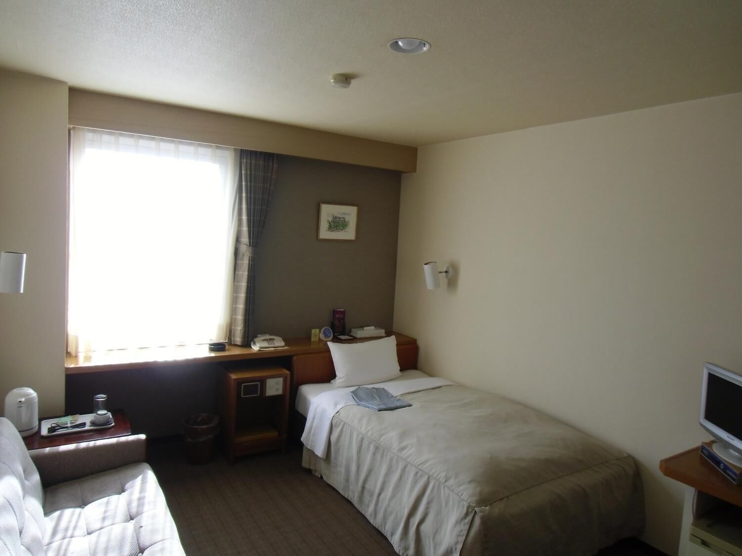 A hotel room with a bed, a desk, a chair, a television, and a window with curtains.
