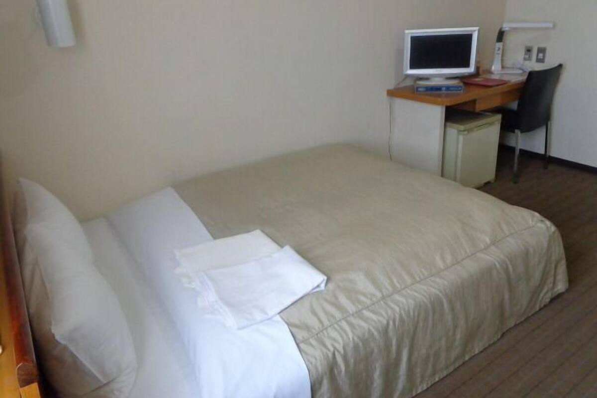 A hotel room with a bed, a desk with a computer, and a chair.