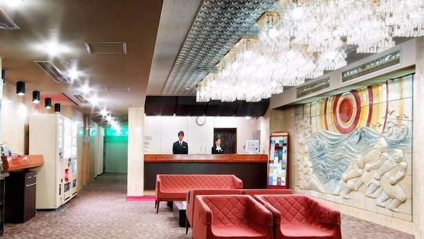 A hotel lobby with a reception desk, red seating, a decorative wall, and a patterned floor. - Hotel Il Viale Hachinohe (Hachinohe)
