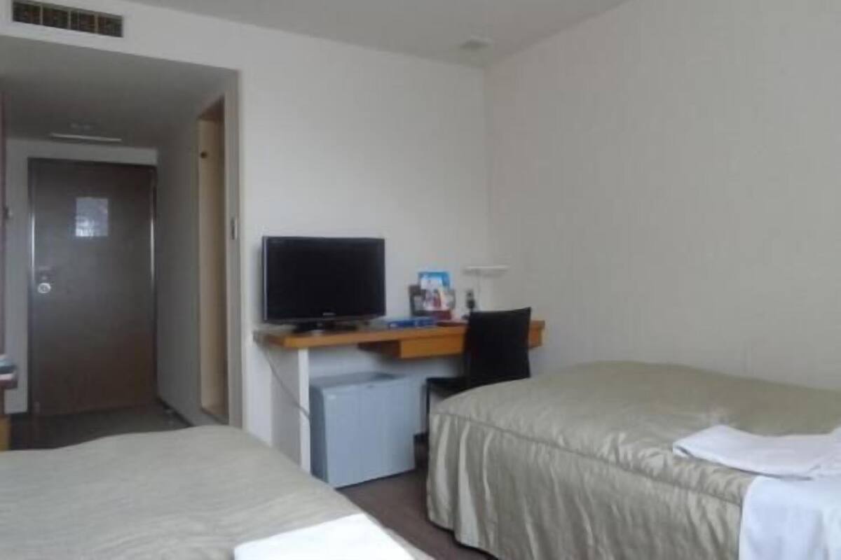 A hotel room with two beds, a desk with a television, and a small refrigerator.