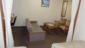 A hotel room with a bed, a sofa, a chair, a small table, and a painting on the wall. - Hotel Il Viale Hachinohe (Hachinohe)