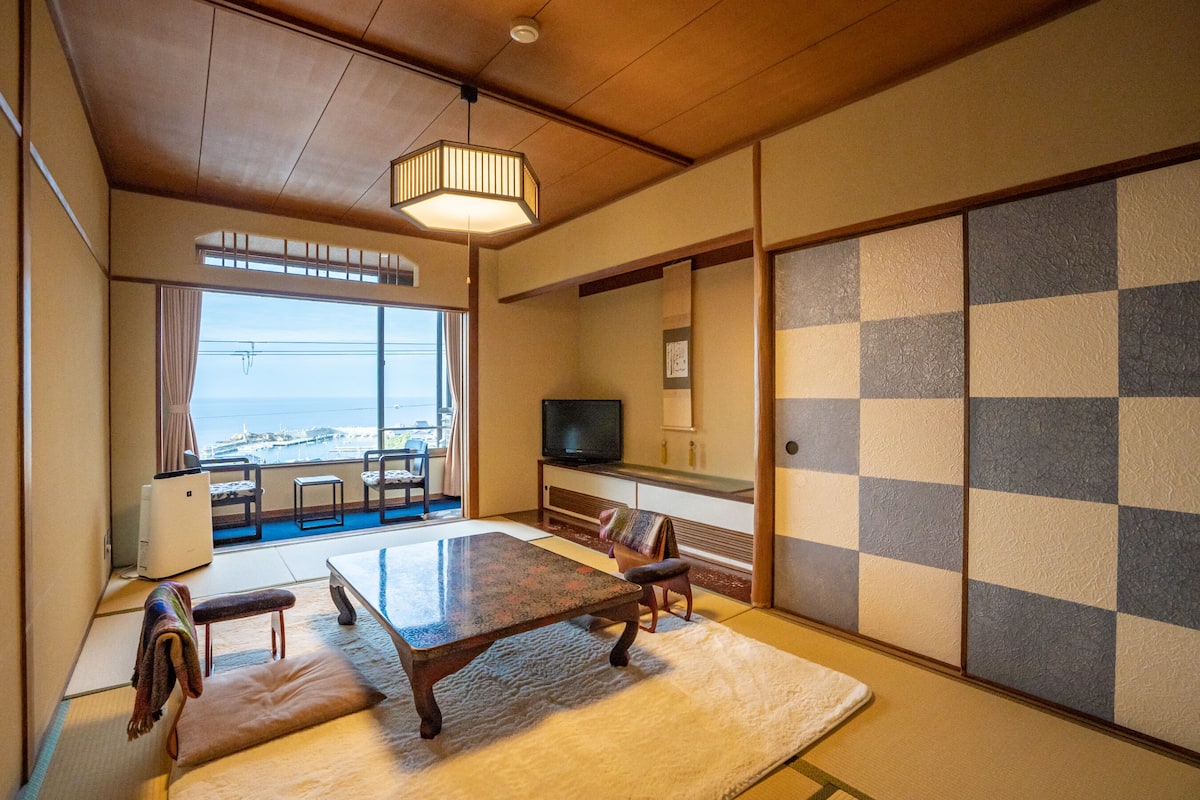 Een traditionele Japanse kamer met tatami vloerbedekking, een salontafel en een televisie op een standaard.