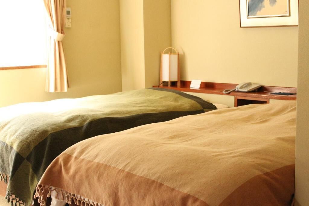 Habitación de hotel con dos camas, una mesita de noche con lámpara, teléfono y un cuadro en la pared.