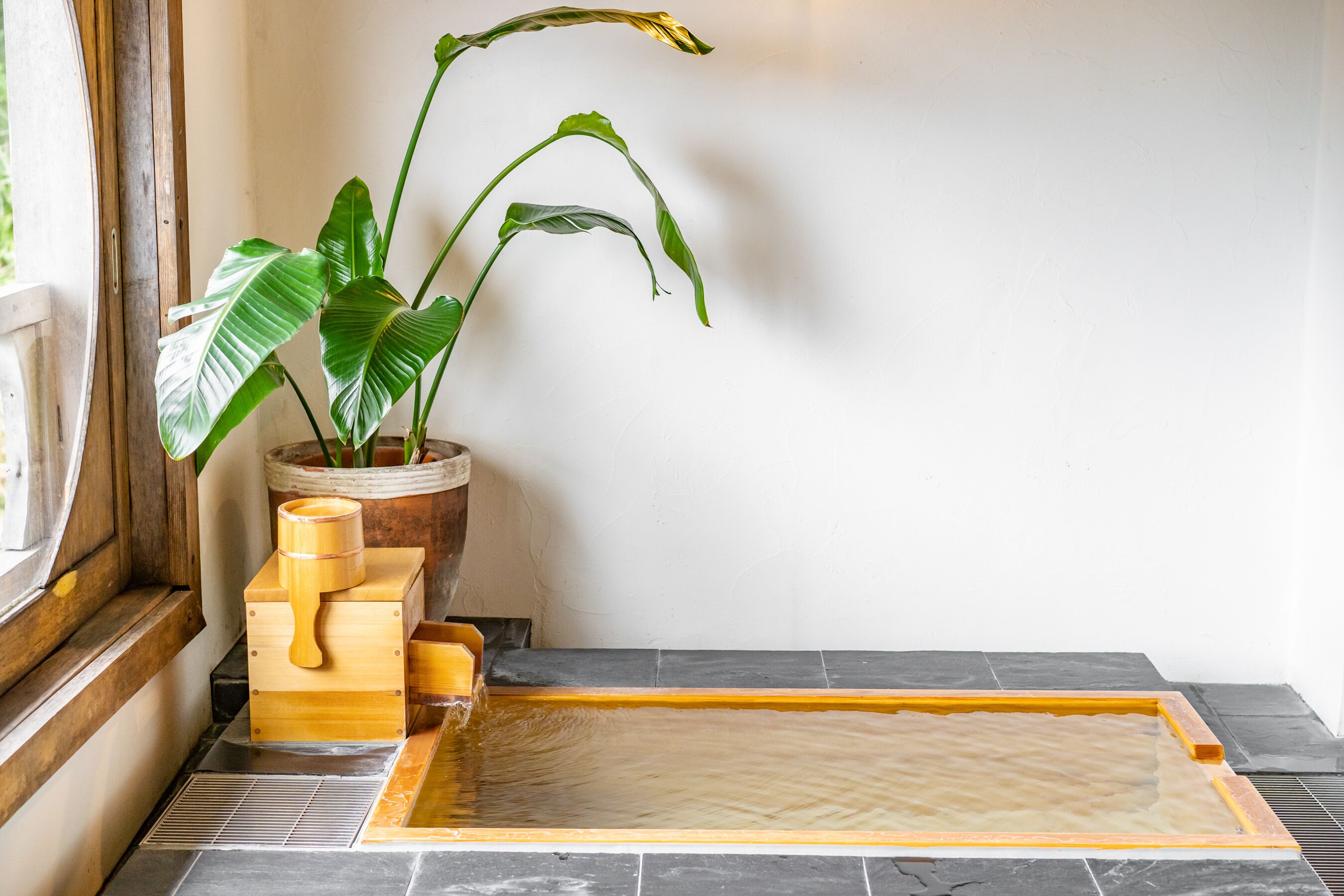 A spa area with a wooden tub, a potted plant, and a tiled floor.