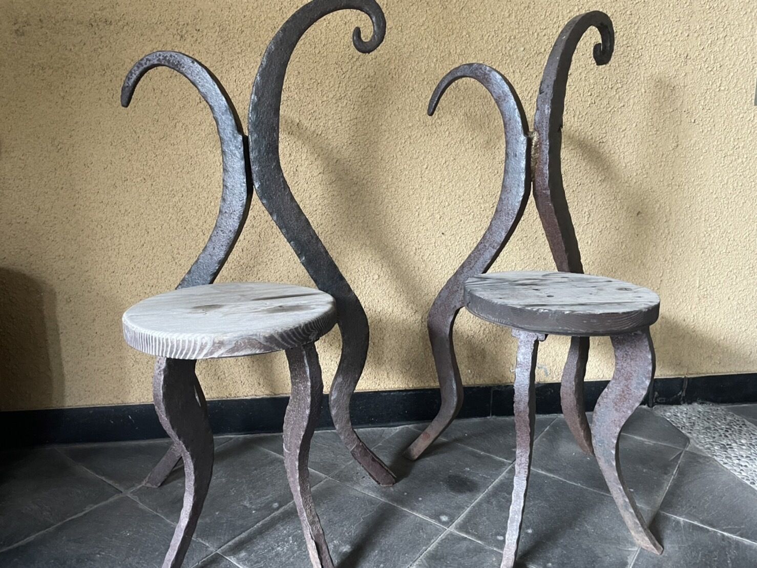 Dos sillas de metal con patas curvas frente a una pared con textura.