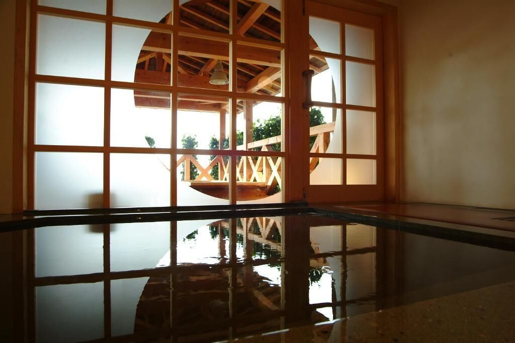 A room with a wooden-framed window with a geometric pattern, a polished floor reflecting the window, and a view of an outdoor wooden structure.