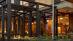 Ein modernes Gebäude mit einer Holz-Pergola, einem Kiesweg und Kübelpflanzen.
