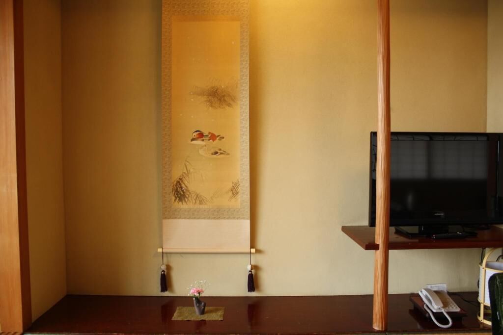 Une pièce avec un bureau en bois, un téléviseur posé sur un meuble et un rouleau de calligraphie traditionnelle accroché au mur.