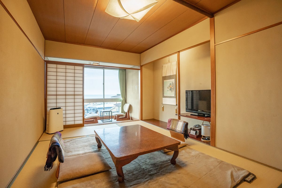 Een traditionele Japanse kamer met tatami vloerbedekking, een lage houten tafel, een televisie en schuifdeuren.