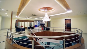 En rummelig lobby med en central trappe, en lysekrone og et moderne loftdesign.