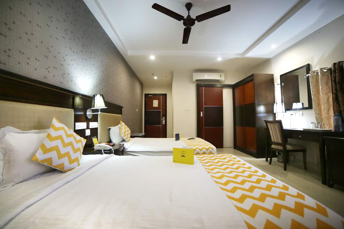 A hotel room with two beds, a desk, a chair, a ceiling fan, and an air conditioning unit.