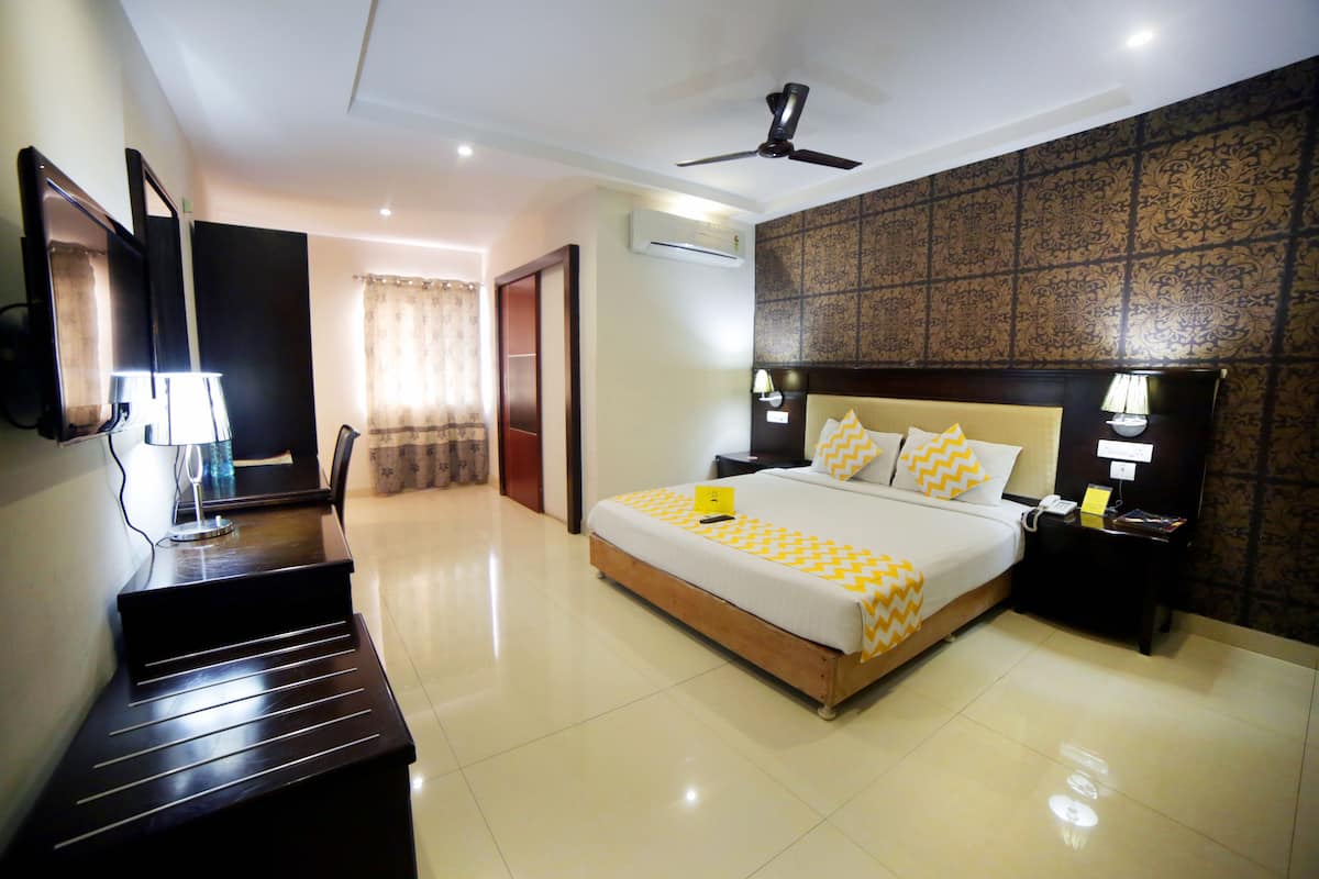 A hotel room with a bed, bedside tables, a desk, a ceiling fan, and an air conditioning unit.