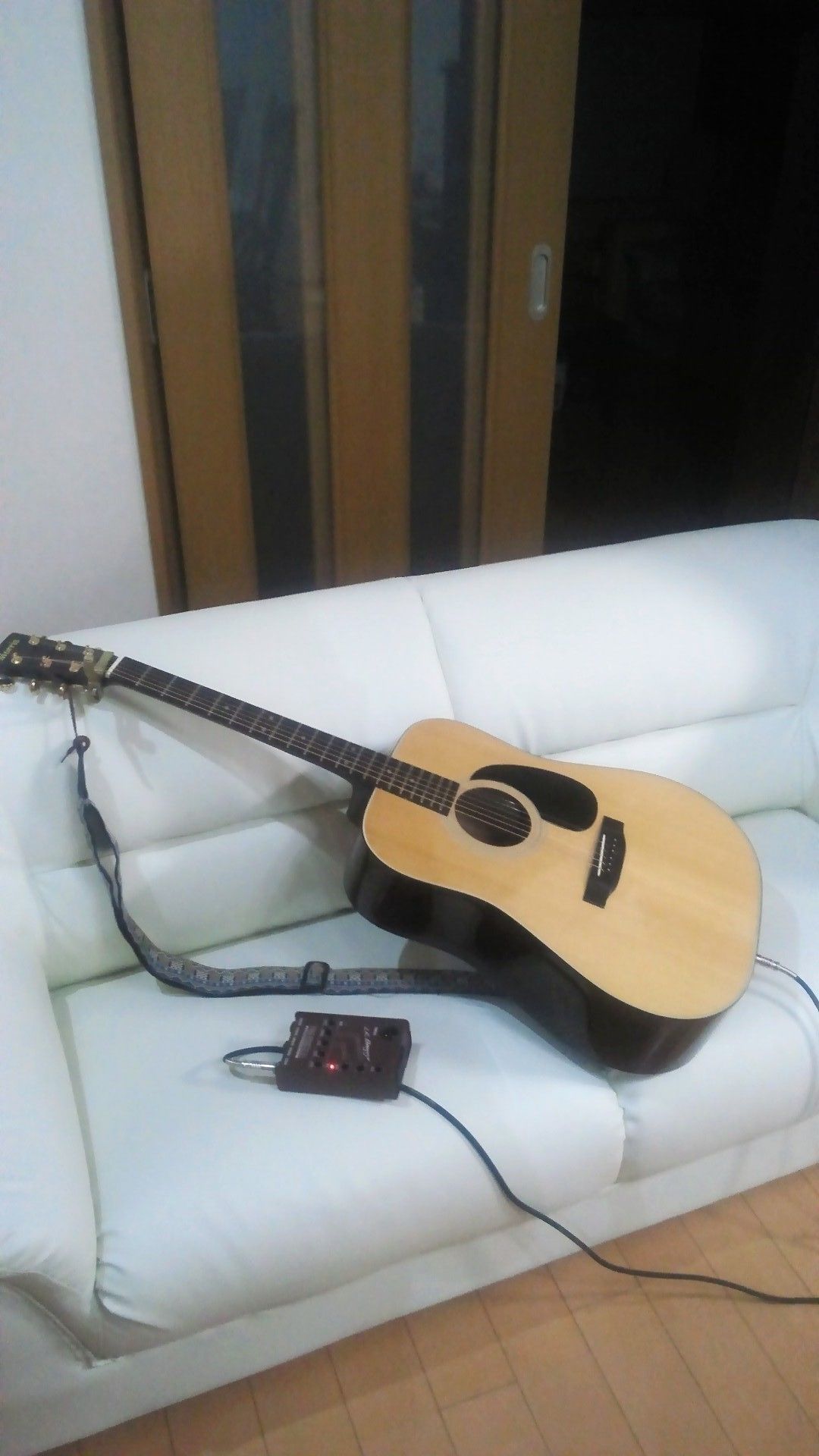 Una guitarra sobre un sofá blanco con un adaptador de corriente enchufado.
