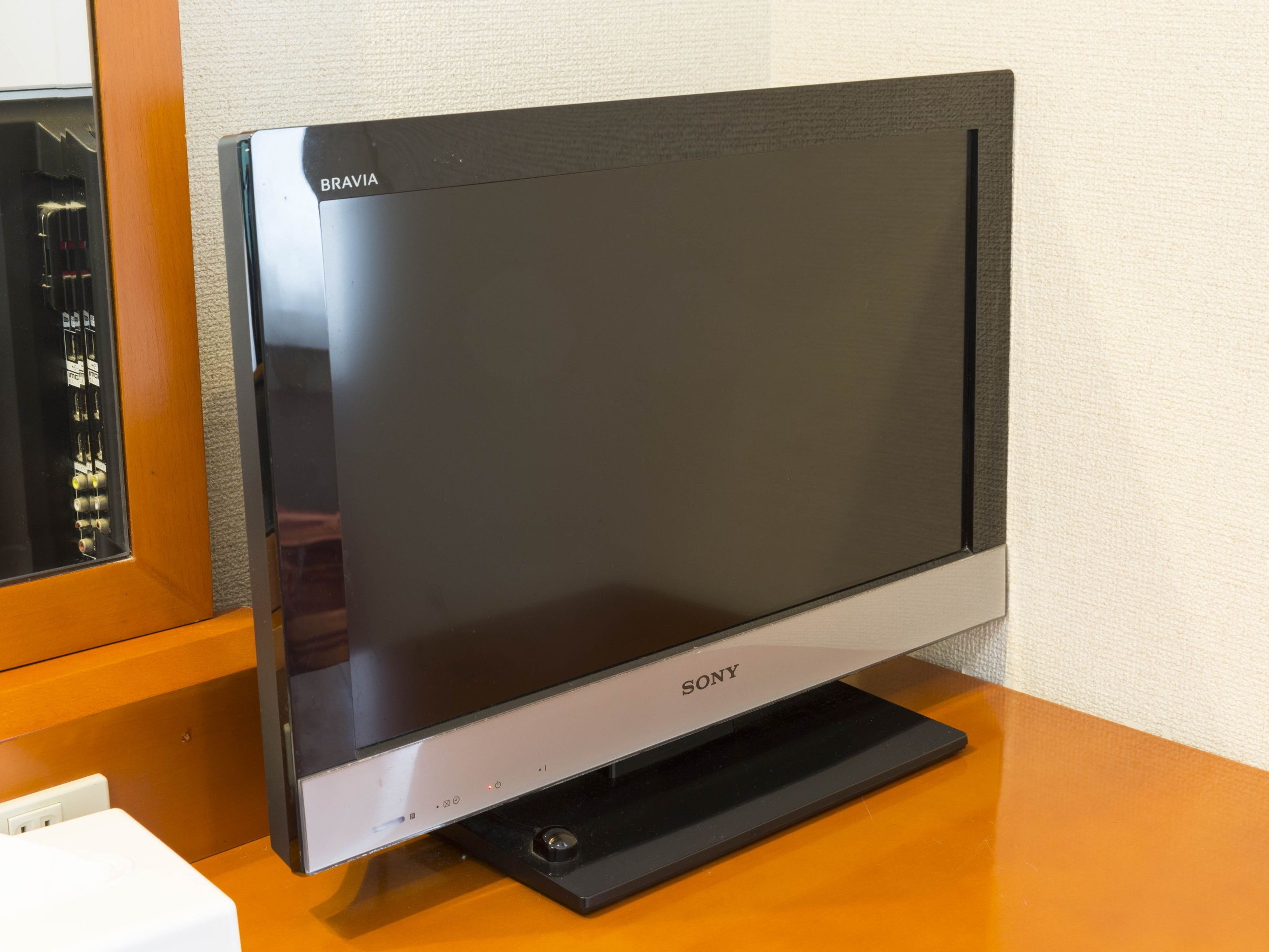 A flat-screen TV on a wooden stand with a power cord plugged in.