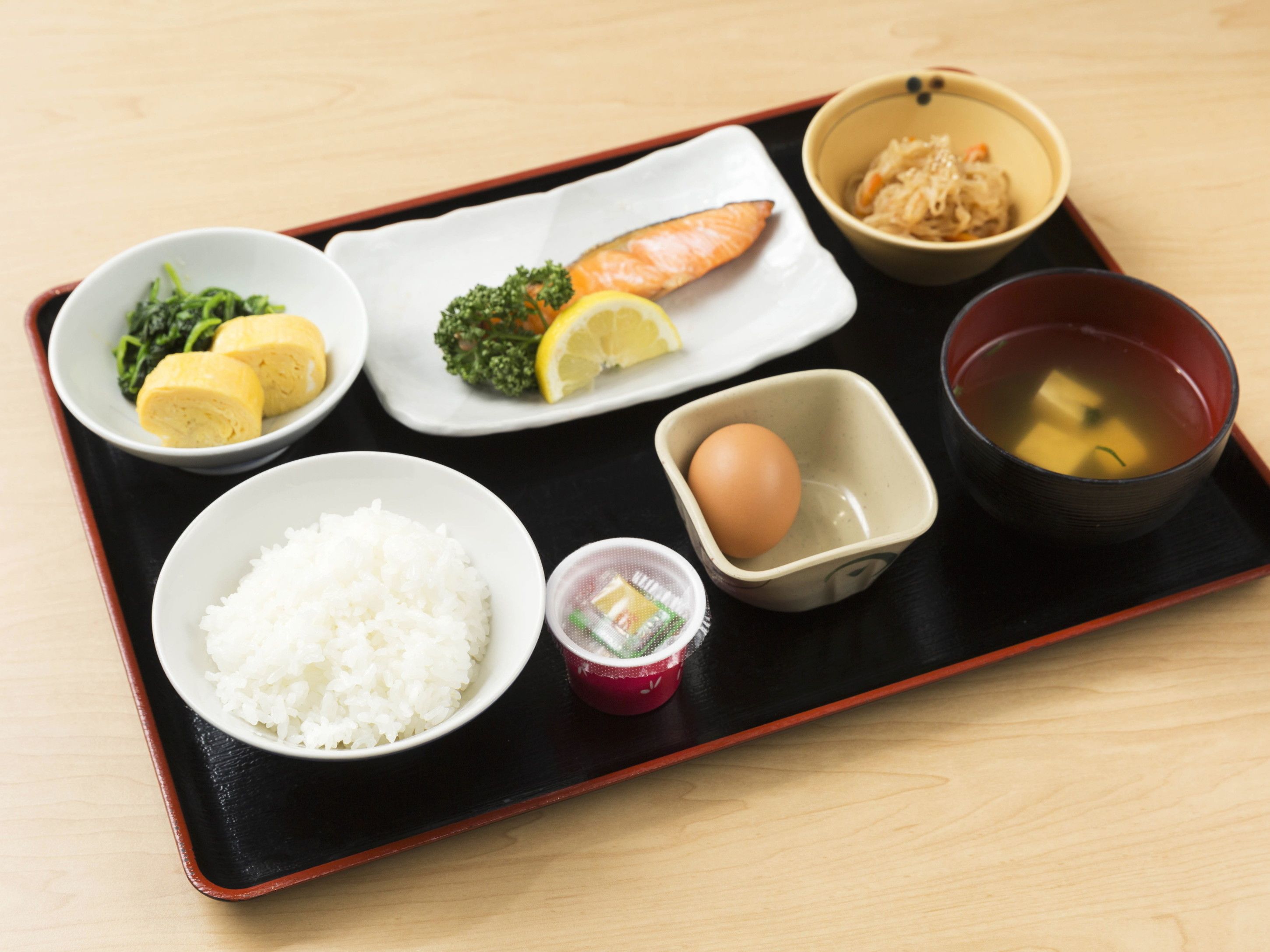 A traditional Japanese meal on a black tray, including rice, salmon, egg, and soup.