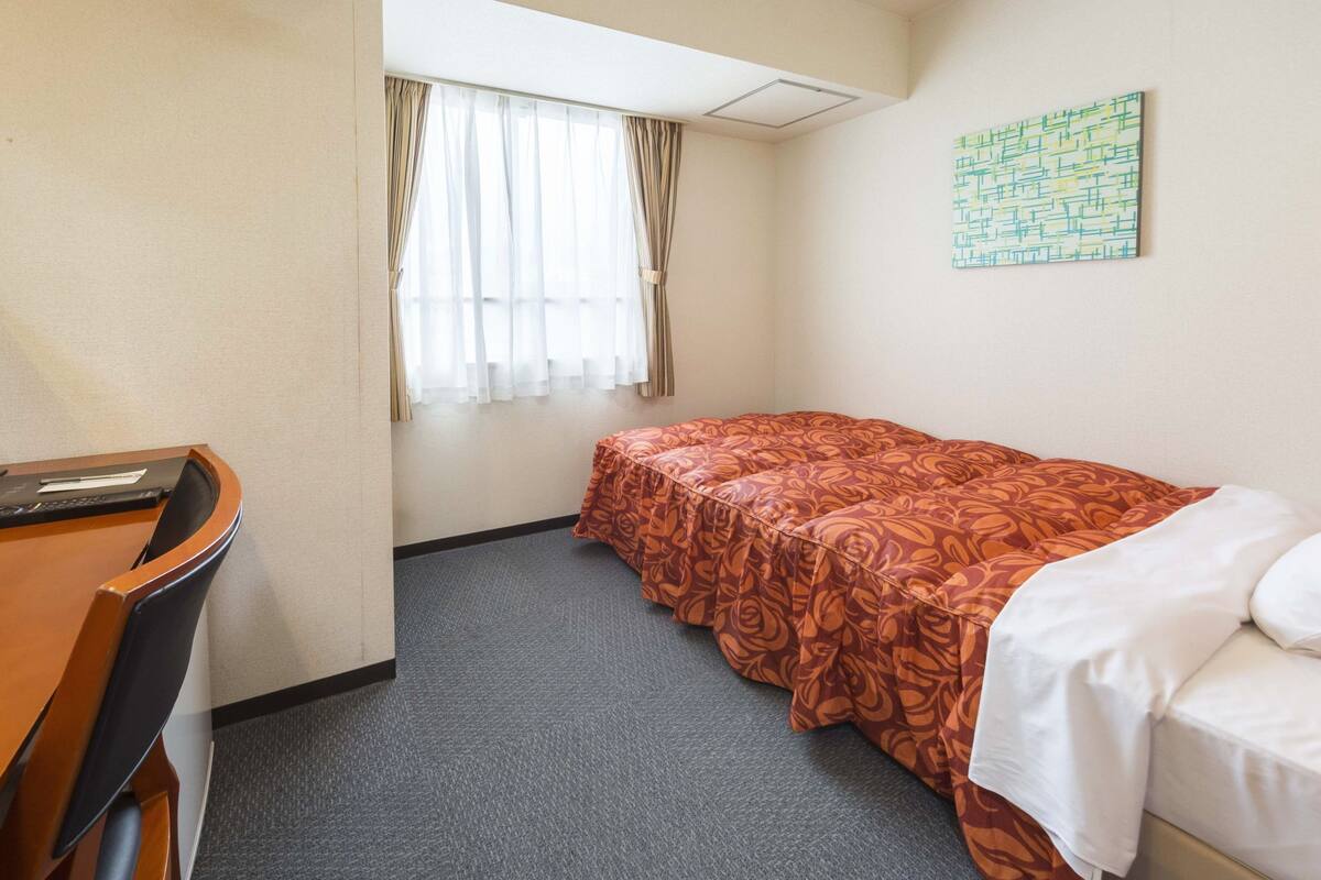 Una habitación de hotel con una cama individual, un escritorio y una ventana con cortinas.