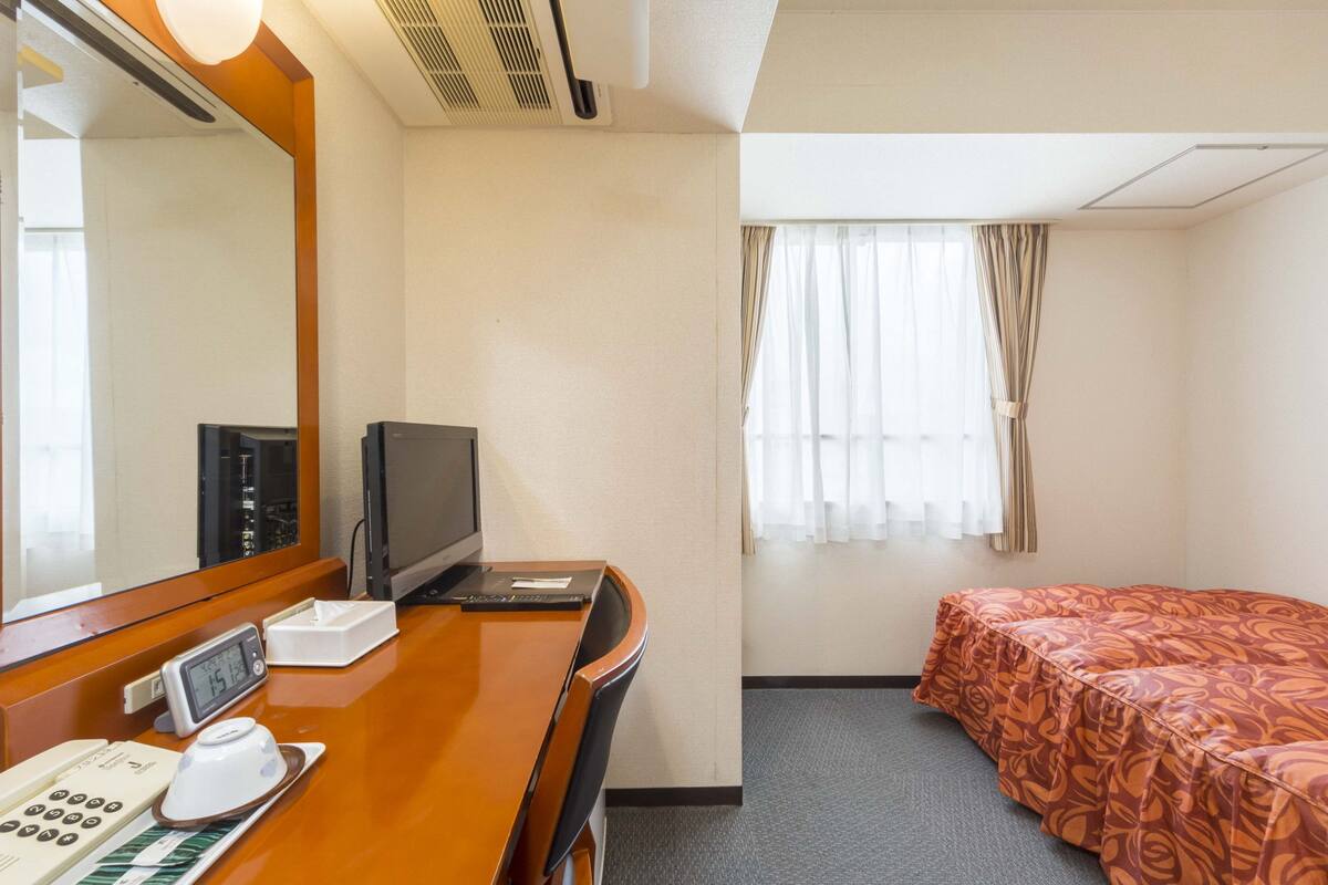 Habitación de hotel con un escritorio de madera, televisor, teléfono y cama con colcha estampada.