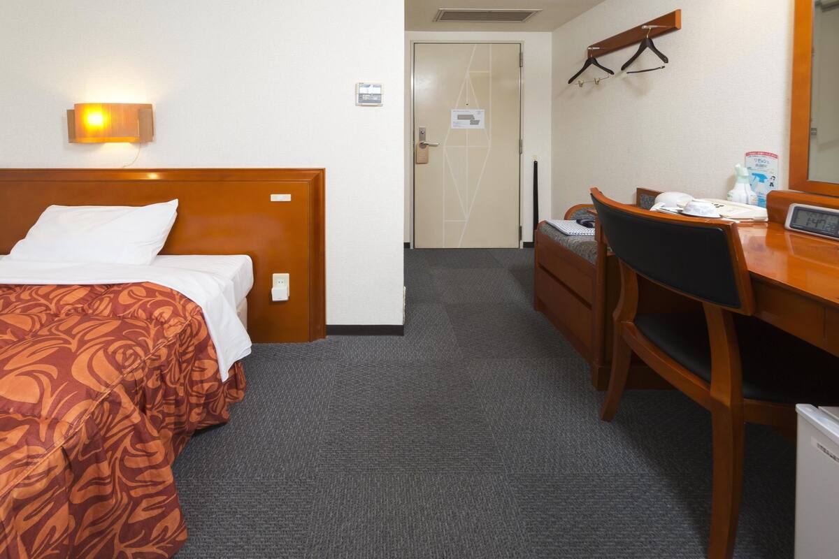 Habitación de hotel con cama, escritorio, silla, refrigerador pequeño y calentador de pared.