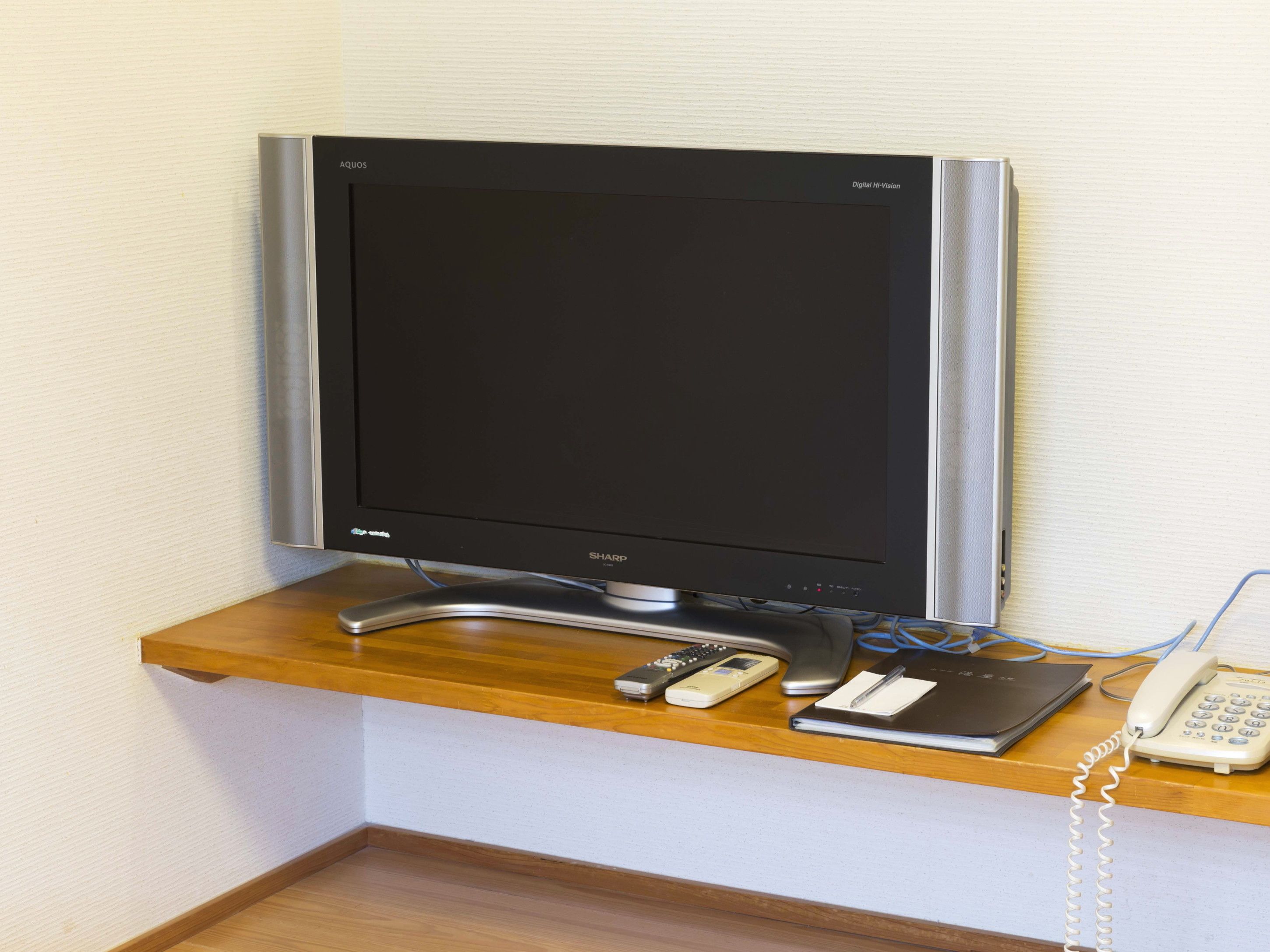 Un téléviseur à écran plat posé sur une étagère en bois, un téléphone et une télécommande.