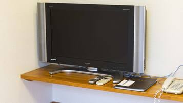 Un téléviseur à écran plat posé sur une étagère en bois, un téléphone et une télécommande.