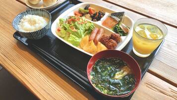 A meal tray with rice, salad, sausages, and soup on a wooden table.